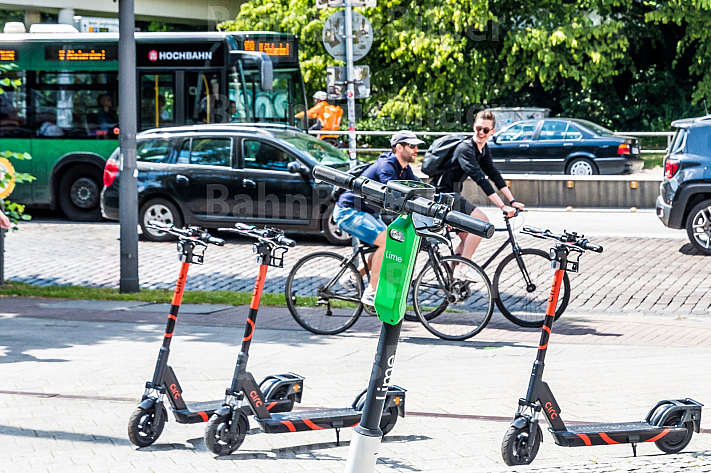 Mehrere E-Scooter verschiedener Leih-Anbieter stehen auf am Dammtor in Hamburg. Im Hintergrund zwei Fahrradfahrer.