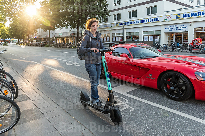 Eine E-Scooter-Fahrerin in der Abendsonne neben einem Auto in der Osterstraße in Hamburg