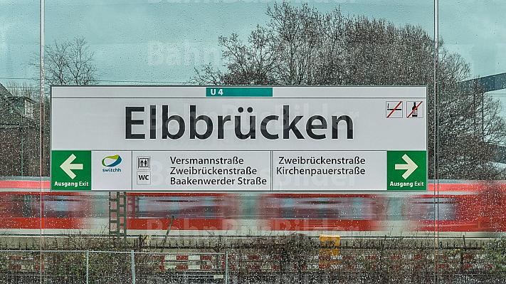 Eine Haltestellenschild im U-Bahnhof Elbbrücken - im Hintergrund eine S-Bahn
