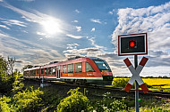 Ein Bahnübergang im Frühling mit Zug und Rapsfeld bei Großenbrode in Schleswig-Holstein