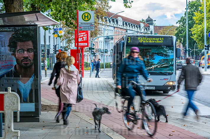Menschen rennen an einer Bushaltestelle in Hamburg zum Bus - eine Radfahrerin kreuzt dabei ihren Weg