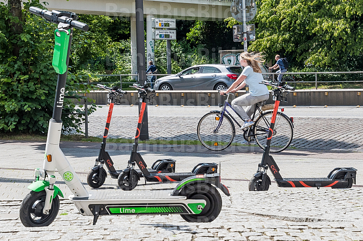 Mehrere E-Scooter verschiedener Leih-Anbieter stehen auf am Dammtor in Hamburg. Im Hintergrund eine Fahrradfahrerin